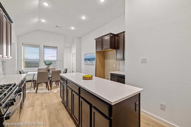 kitchen featuring light hardwood / wood-style flooring, stainless steel gas range, dark brown cabinets, a kitchen island, and vaulted ceiling