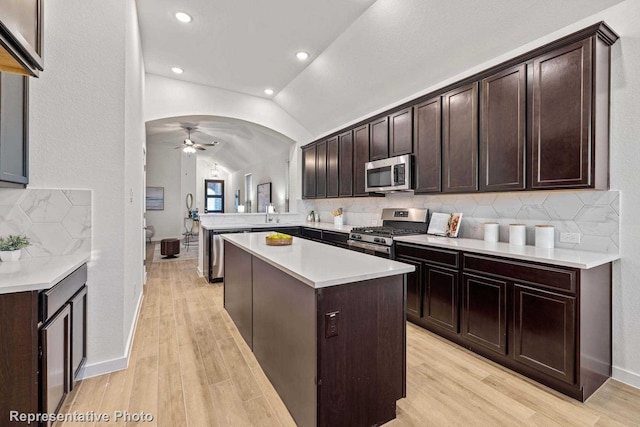 kitchen featuring vaulted ceiling, appliances with stainless steel finishes, kitchen peninsula, a kitchen island, and light hardwood / wood-style floors