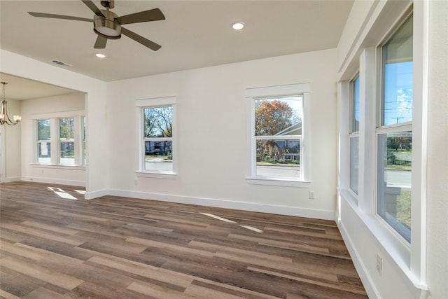 empty room featuring ceiling fan with notable chandelier and dark hardwood / wood-style floors