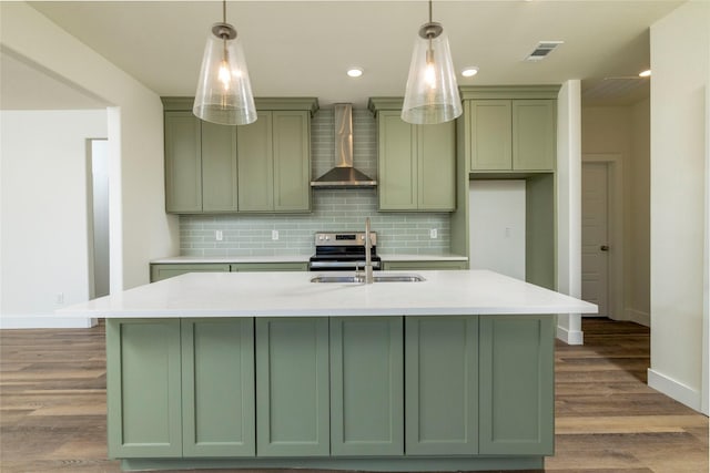 kitchen with sink, light hardwood / wood-style flooring, wall chimney range hood, and a center island with sink