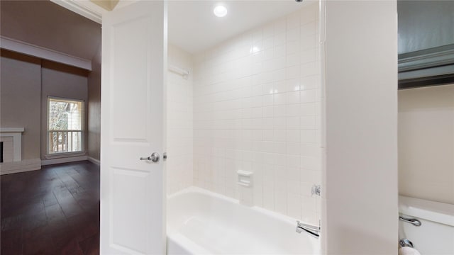 bathroom with a fireplace, hardwood / wood-style floors, tiled shower / bath combo, and toilet