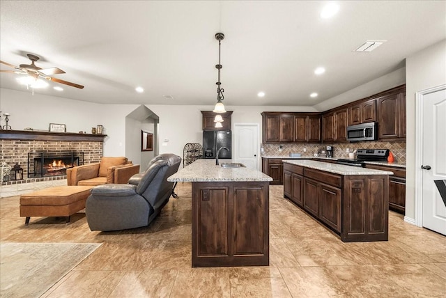 kitchen featuring a center island with sink, dark brown cabinetry, hanging light fixtures, and appliances with stainless steel finishes