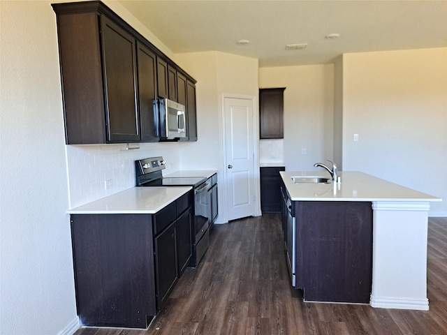 kitchen with dark wood-type flooring, sink, stainless steel appliances, and a center island with sink