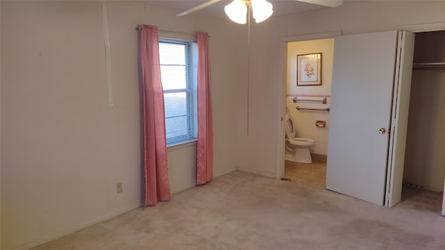 unfurnished bedroom with a closet, light colored carpet, ensuite bath, and ceiling fan