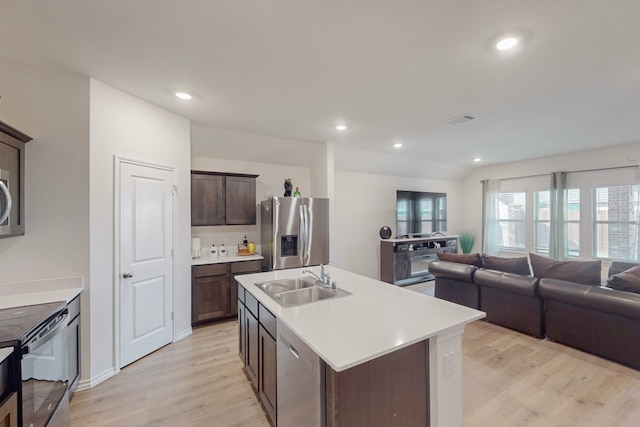 kitchen featuring appliances with stainless steel finishes, dark brown cabinets, sink, a center island with sink, and light hardwood / wood-style flooring