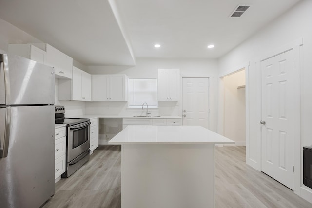 kitchen with stainless steel appliances, a sink, a kitchen island, white cabinetry, and light countertops