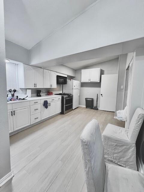 kitchen with vaulted ceiling, white cabinetry, and gas range