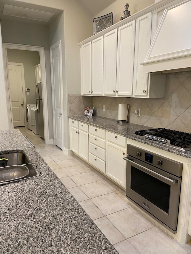 kitchen featuring premium range hood, decorative backsplash, light tile patterned floors, white cabinetry, and stainless steel appliances