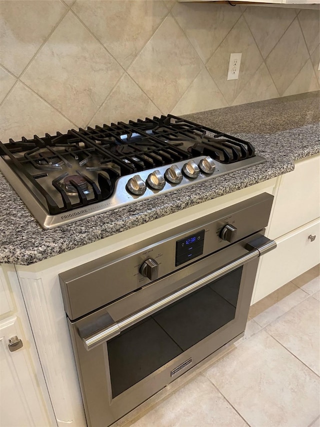 interior details with appliances with stainless steel finishes, backsplash, and white cabinetry