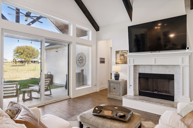 living room featuring beam ceiling, ceiling fan, high vaulted ceiling, a tiled fireplace, and hardwood / wood-style flooring