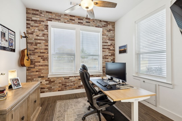 home office with ceiling fan, dark hardwood / wood-style floors, a healthy amount of sunlight, and brick wall