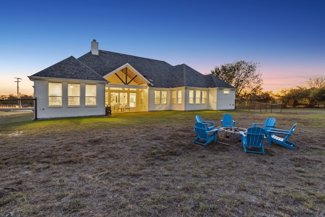 back house at dusk featuring a lawn and an outdoor fire pit