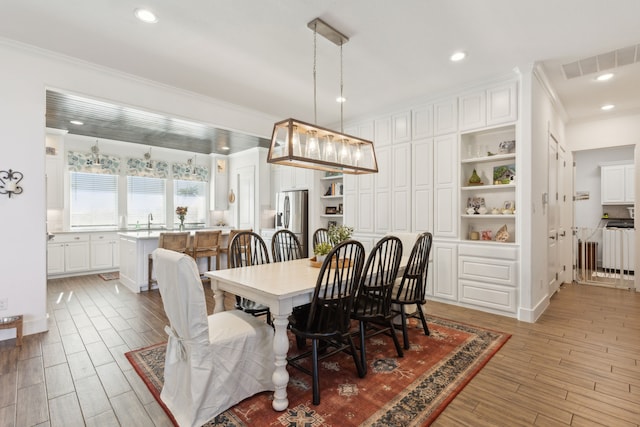 dining area with sink, wood-type flooring, and ornamental molding