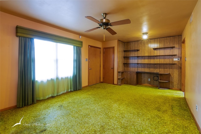 unfurnished living room with light carpet, ceiling fan, and wood walls