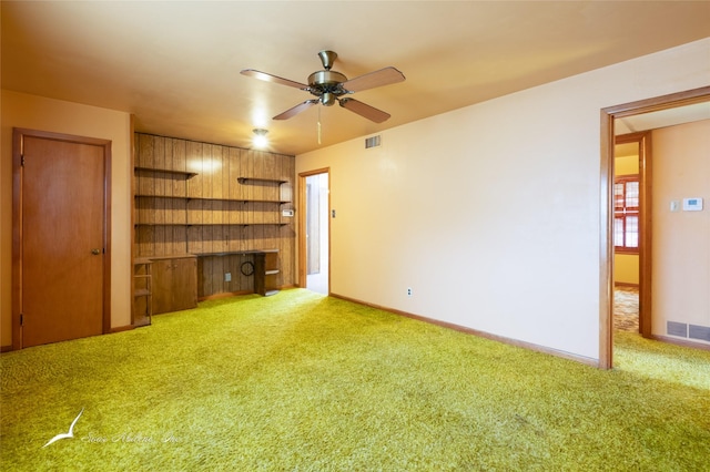 unfurnished living room with ceiling fan, wooden walls, and carpet floors