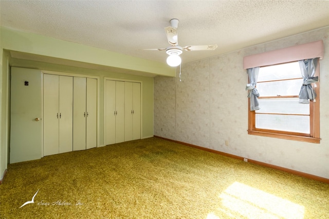 unfurnished bedroom with carpet flooring, two closets, ceiling fan, and a textured ceiling