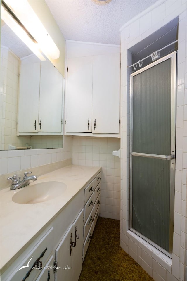 bathroom featuring vanity, decorative backsplash, a textured ceiling, tile walls, and an enclosed shower