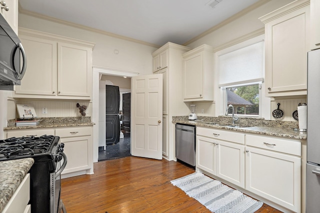 kitchen with light stone countertops, appliances with stainless steel finishes, crown molding, sink, and dark hardwood / wood-style floors