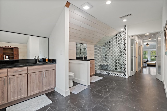 bathroom featuring walk in shower, vanity, toilet, and tile walls