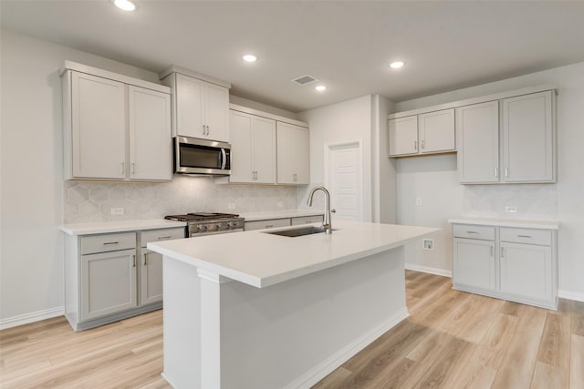 kitchen with light hardwood / wood-style floors, sink, stainless steel appliances, and an island with sink