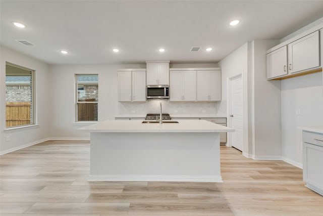 kitchen featuring light wood-type flooring, a center island with sink, and white cabinetry