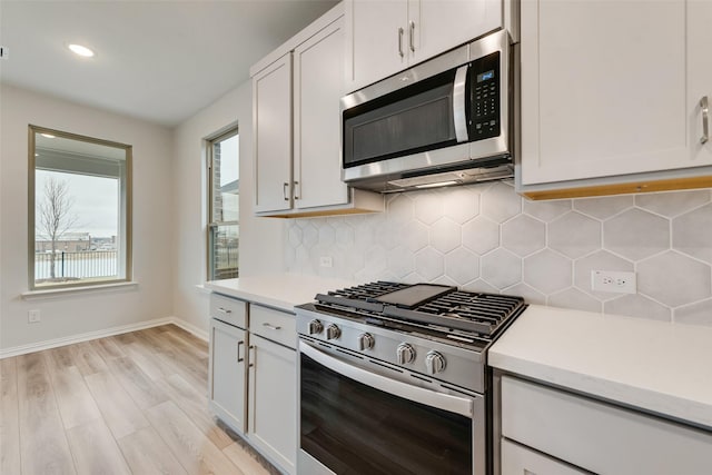 kitchen with backsplash, white cabinets, light wood-type flooring, and appliances with stainless steel finishes