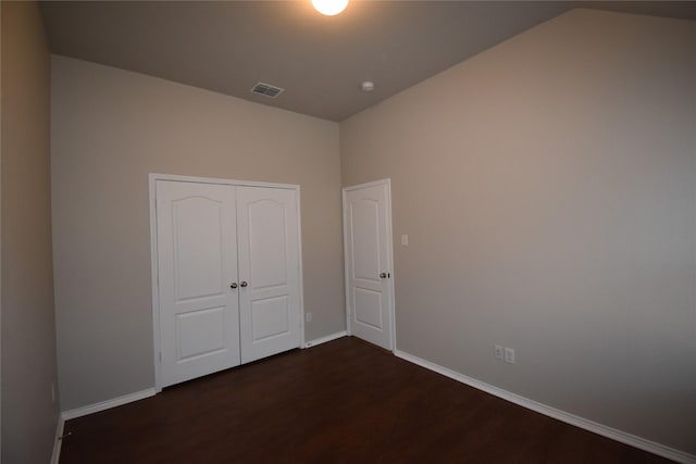 unfurnished bedroom featuring lofted ceiling, dark hardwood / wood-style floors, and a closet