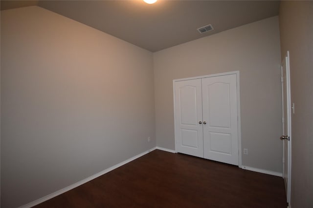 unfurnished bedroom featuring dark wood-type flooring, a closet, and vaulted ceiling