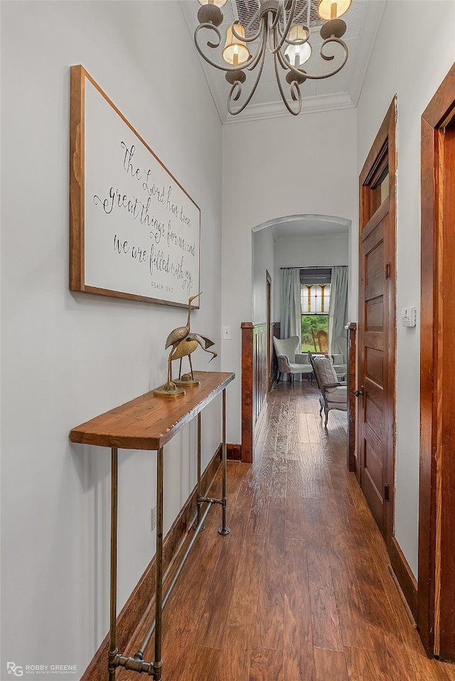 hallway with arched walkways, dark wood-style flooring, crown molding, a chandelier, and baseboards