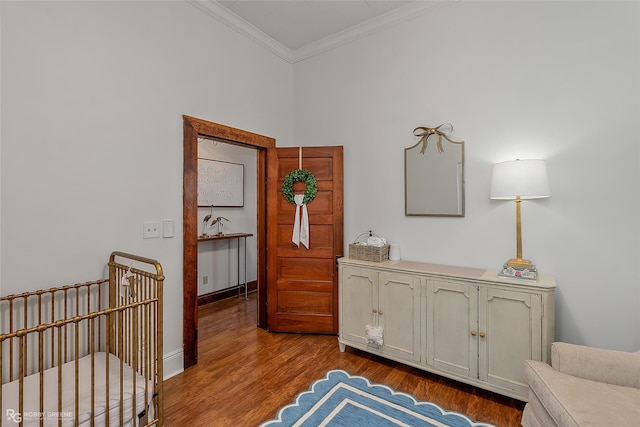 interior space featuring crown molding, a crib, baseboards, and wood finished floors