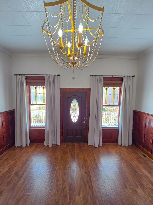 foyer with a wainscoted wall, plenty of natural light, wood finished floors, and an inviting chandelier