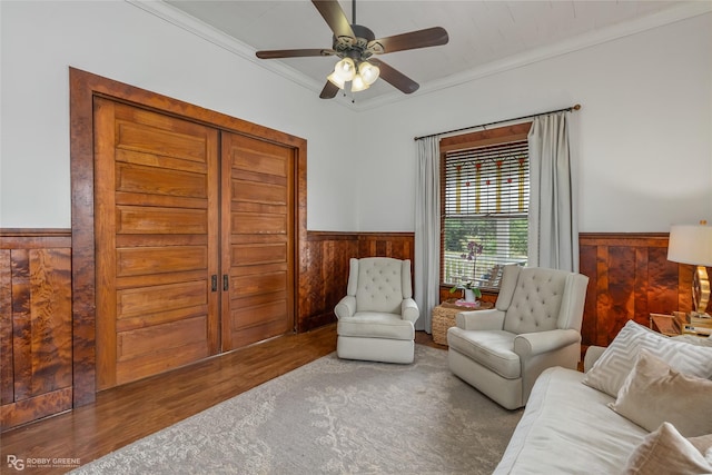 living area with wainscoting, crown molding, wood walls, and wood finished floors