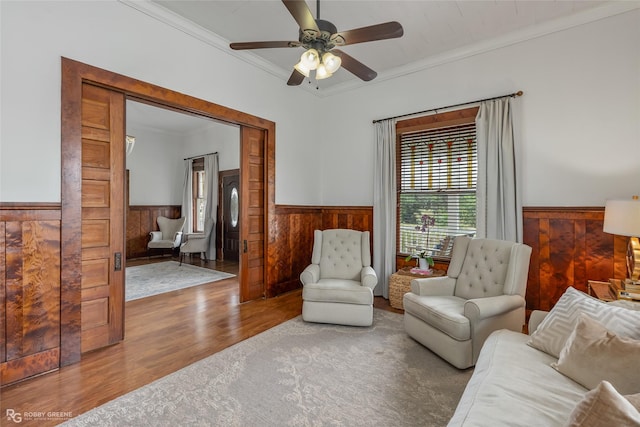 living room featuring a wainscoted wall, ceiling fan, wood finished floors, and crown molding