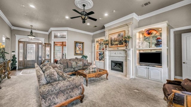 carpeted living room featuring a tiled fireplace, ornamental molding, and ceiling fan