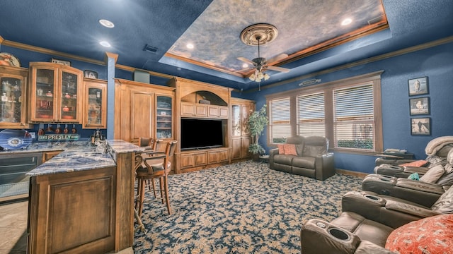 carpeted living room with crown molding, bar area, a textured ceiling, a raised ceiling, and ceiling fan