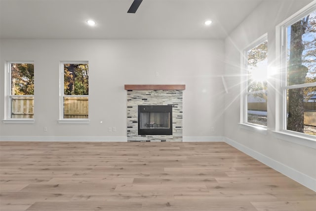 unfurnished living room with ceiling fan, a tile fireplace, and light wood-type flooring