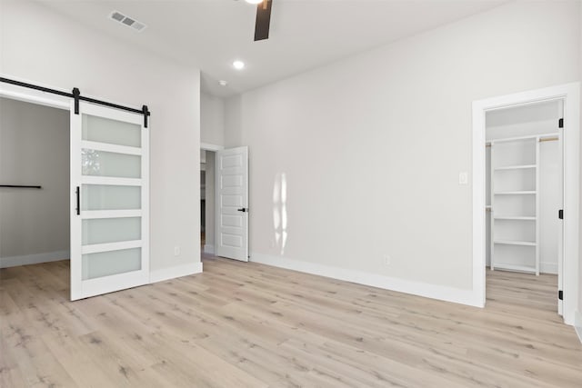 unfurnished bedroom featuring a closet, a walk in closet, light hardwood / wood-style floors, and a barn door