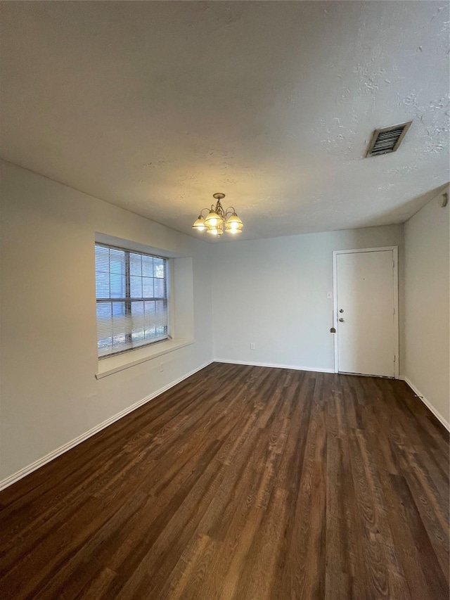 empty room with a chandelier and dark wood-type flooring