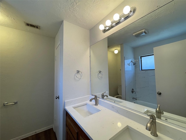 full bathroom featuring vanity, a textured ceiling, tiled shower / bath combo, hardwood / wood-style flooring, and toilet