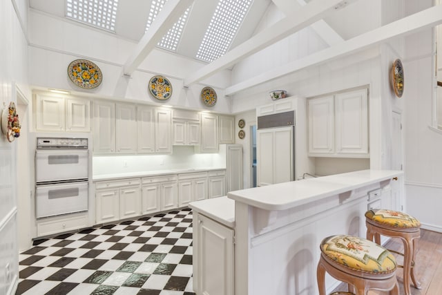 kitchen with beam ceiling, white double oven, paneled refrigerator, a breakfast bar, and white cabinets