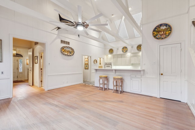 unfurnished living room with beam ceiling, high vaulted ceiling, light hardwood / wood-style flooring, and ceiling fan