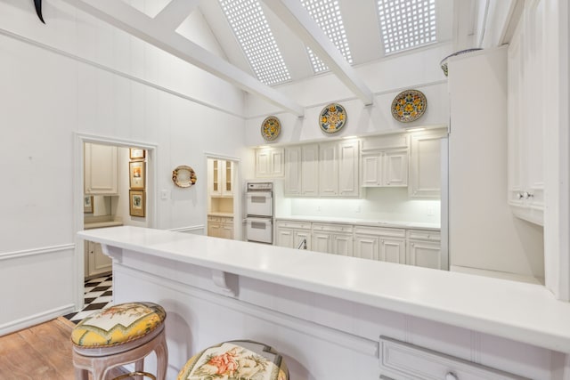 kitchen with kitchen peninsula, double oven, light hardwood / wood-style flooring, white cabinetry, and lofted ceiling