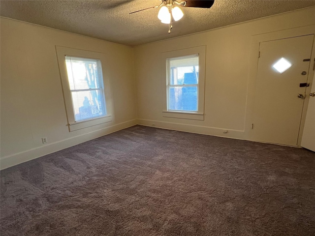 unfurnished room featuring a textured ceiling, dark carpet, plenty of natural light, and ceiling fan