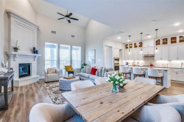 dining room with high vaulted ceiling, a fireplace, sink, ceiling fan, and light hardwood / wood-style flooring