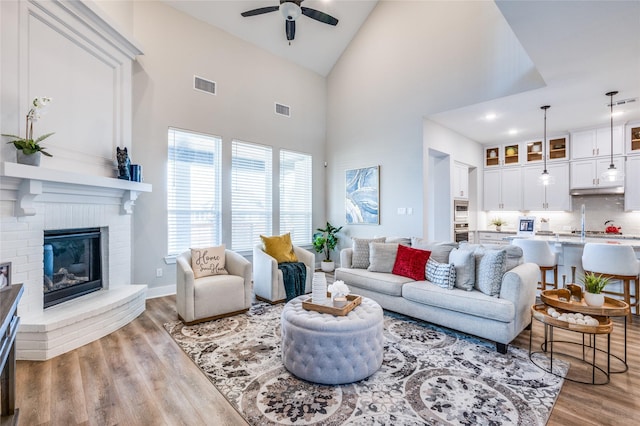 living room with ceiling fan, a fireplace, high vaulted ceiling, and light hardwood / wood-style flooring