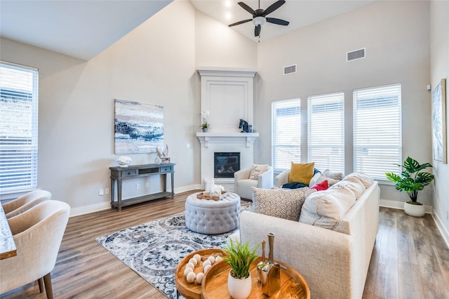 living room featuring a brick fireplace, wood-type flooring, high vaulted ceiling, and ceiling fan