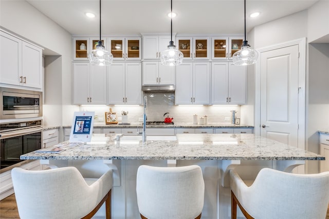 kitchen featuring a center island with sink, appliances with stainless steel finishes, pendant lighting, and white cabinets