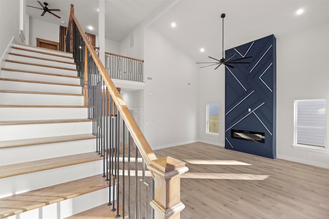 staircase featuring hardwood / wood-style floors, high vaulted ceiling, and ceiling fan