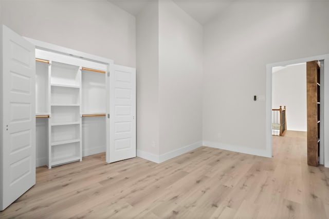 unfurnished bedroom with a closet, a towering ceiling, and light hardwood / wood-style floors