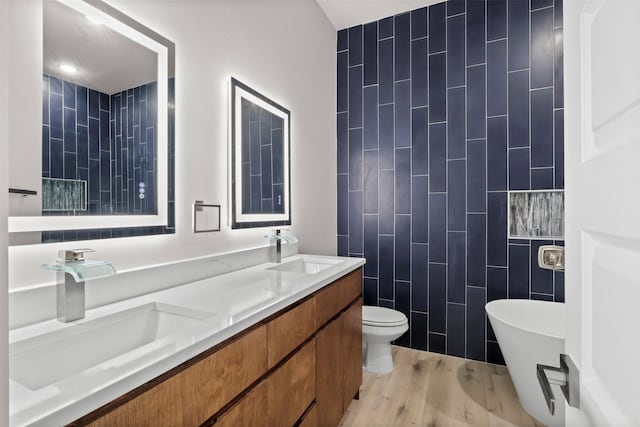 bathroom with a bathing tub, hardwood / wood-style floors, toilet, vanity, and tile walls